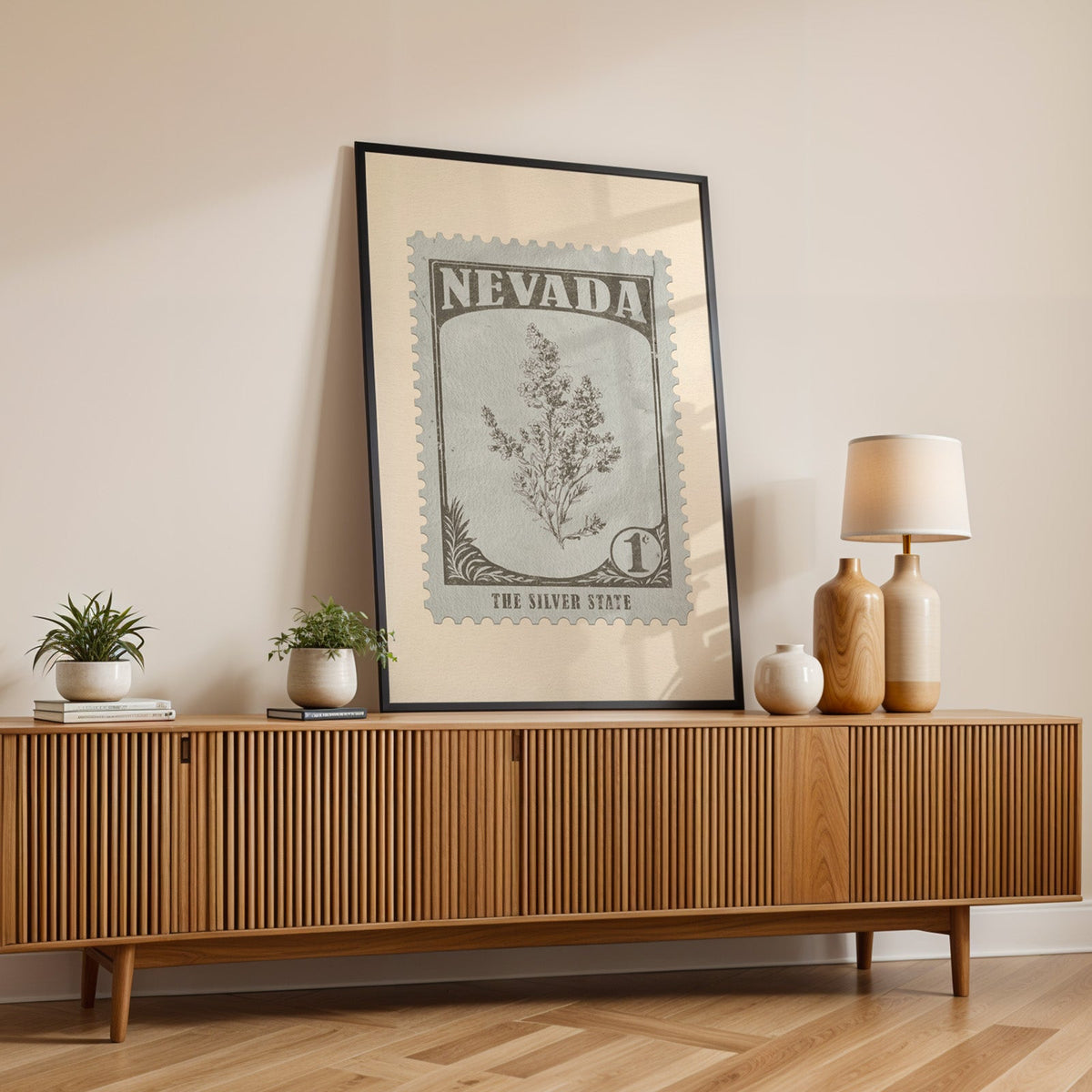 Nevada state flower print in a black frame leaning on a fluted wood credenza with vases and a lamp
