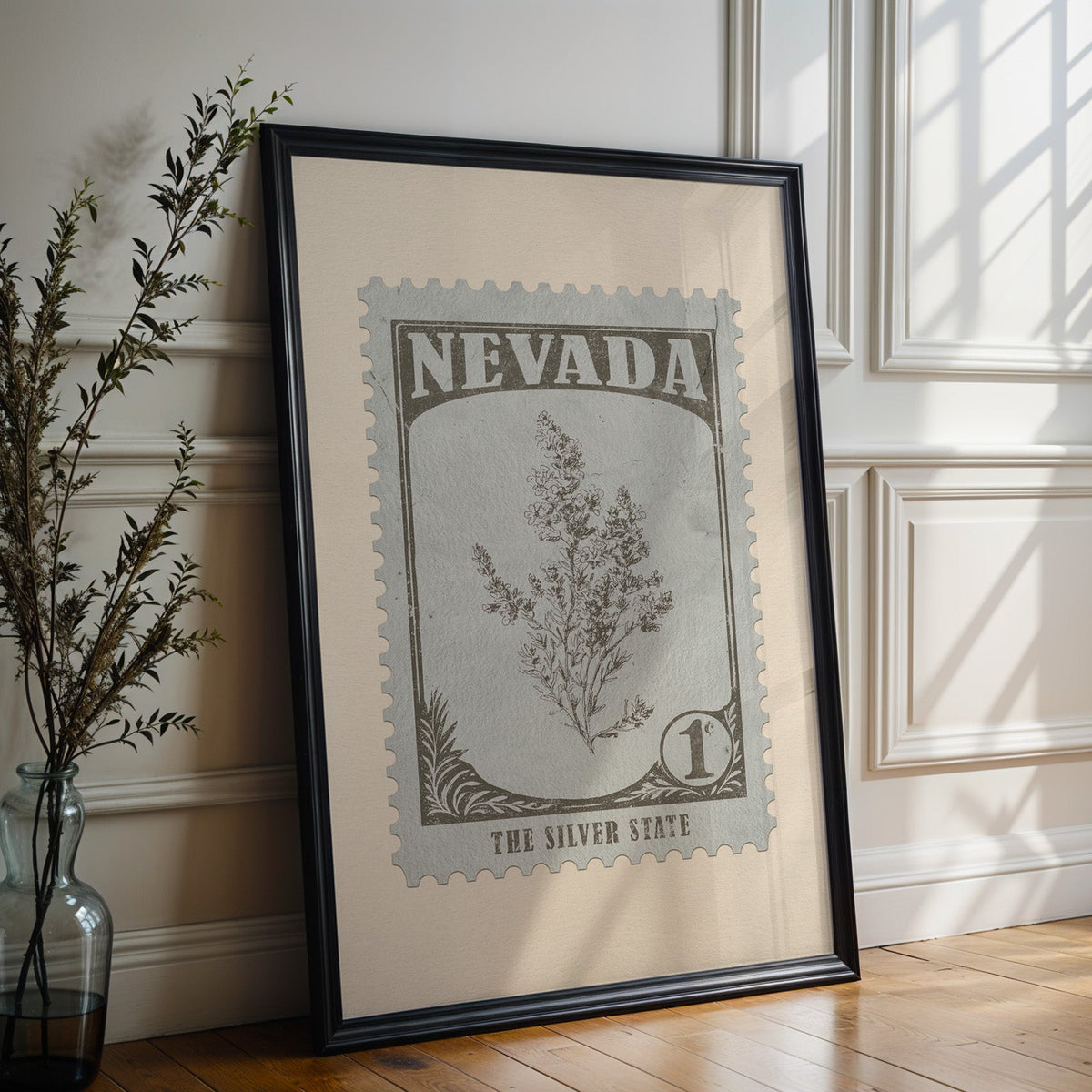 Nevada state flower print in a black frame leaning against a white panelled wall beside olive branches