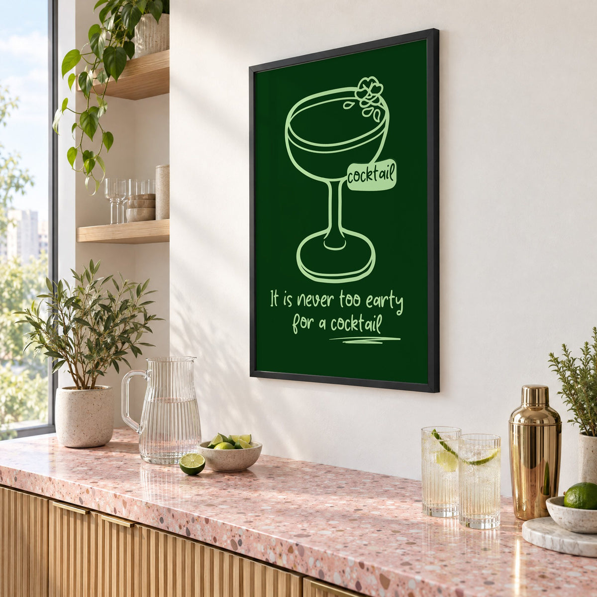 Never too early cocktail coupe print in a black frame above a pink terrazzo cocktail counter with limes, seen at an angle