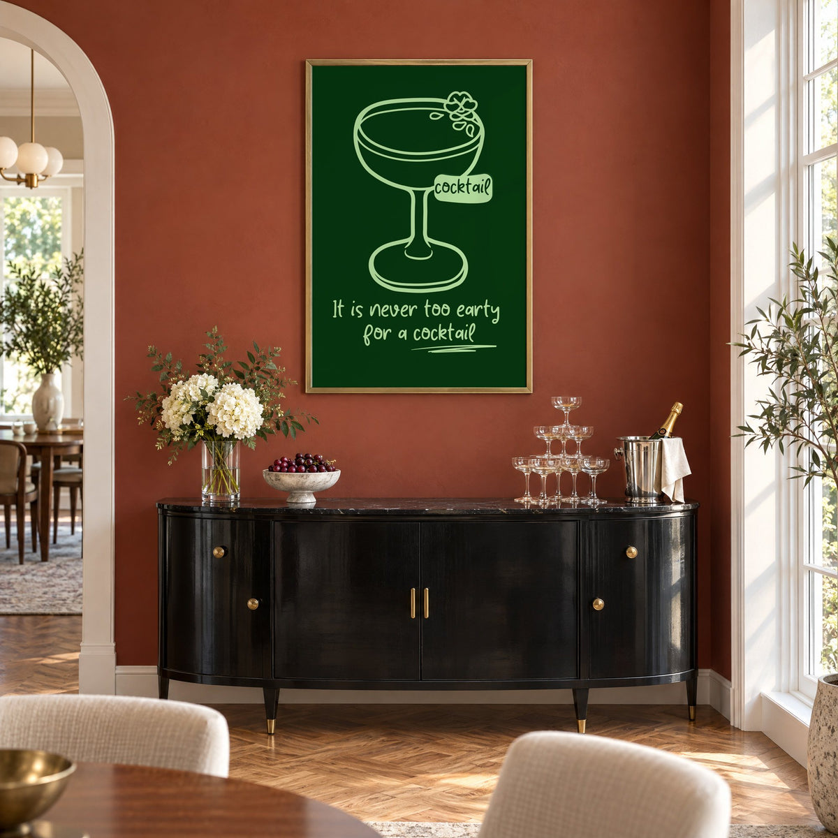 Never too early cocktail coupe print in a brass frame on a terracotta wall above a black buffet with a champagne tower