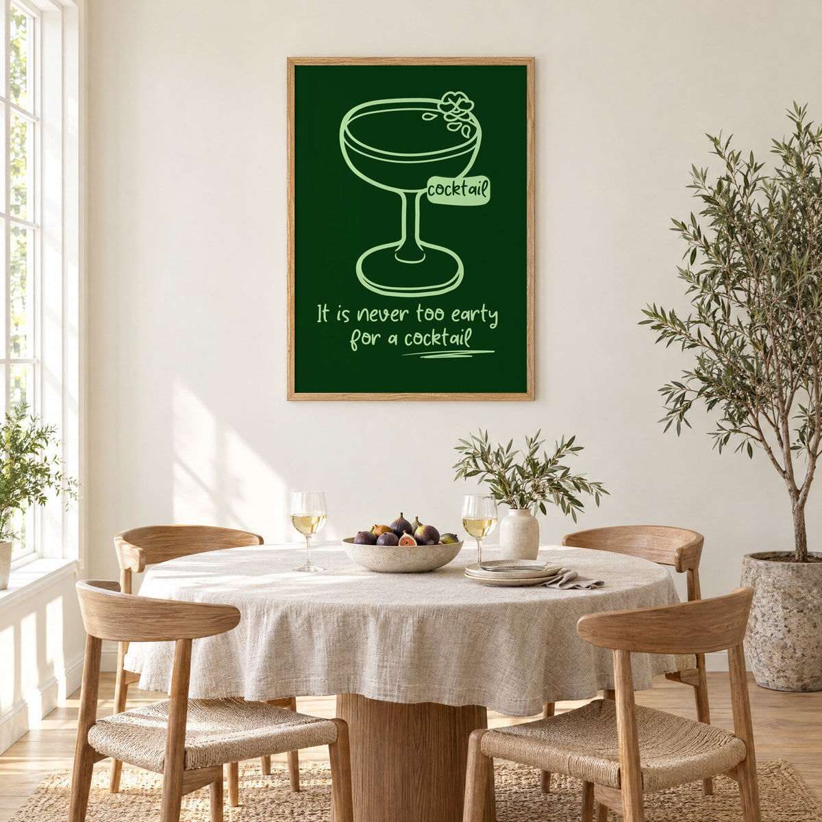 Never too early cocktail coupe print in an oak frame above a round linen-covered dining table with figs and wine