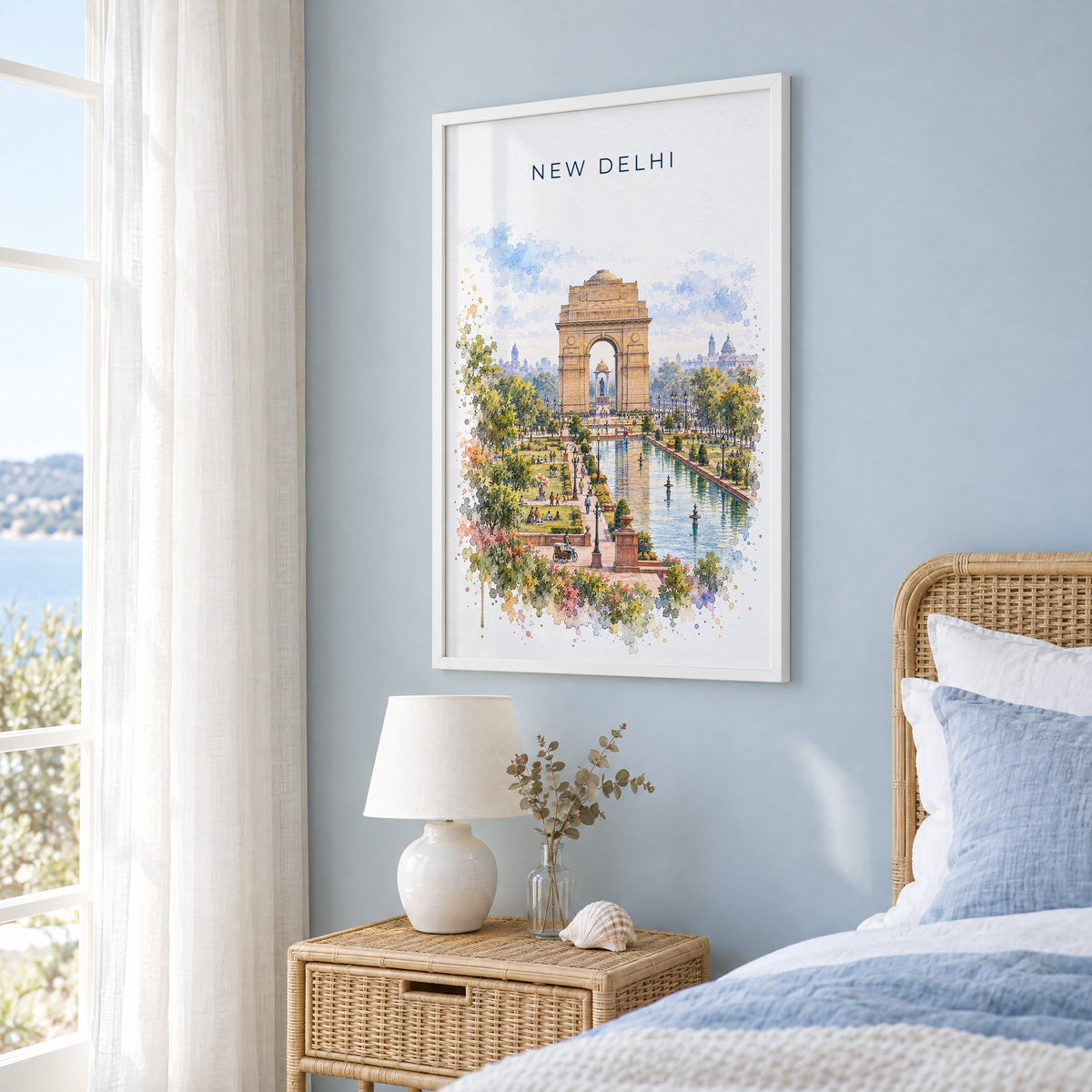 New Delhi watercolor print in a white frame on a pale blue wall beside a rattan bed in a coastal bedroom