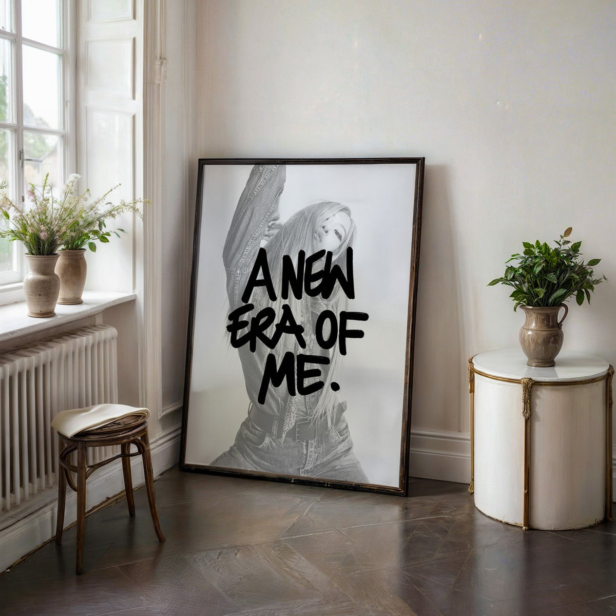 A new era of me lettering over woman in denim print in a black frame on a dark stone floor beside a white side table