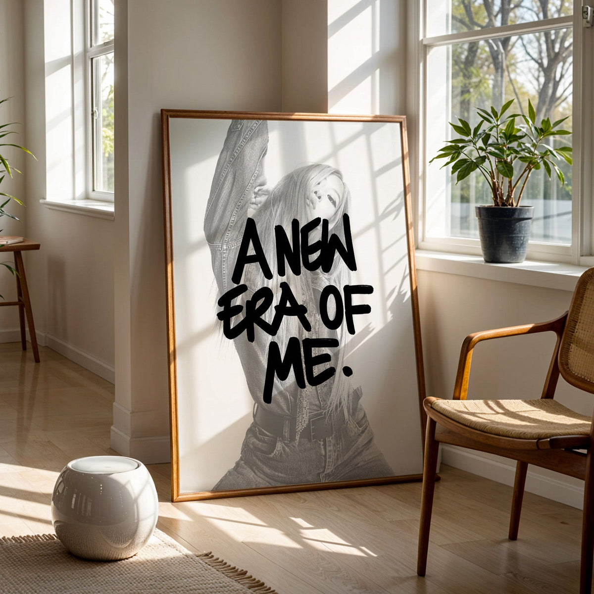 A new era of me lettering over woman in denim print in a walnut frame on a wood floor beside a cane chair and sunny window