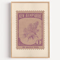 New Hampshire state flower stamp print in mauve purple on rose tan, light oak frame on a plain white wall