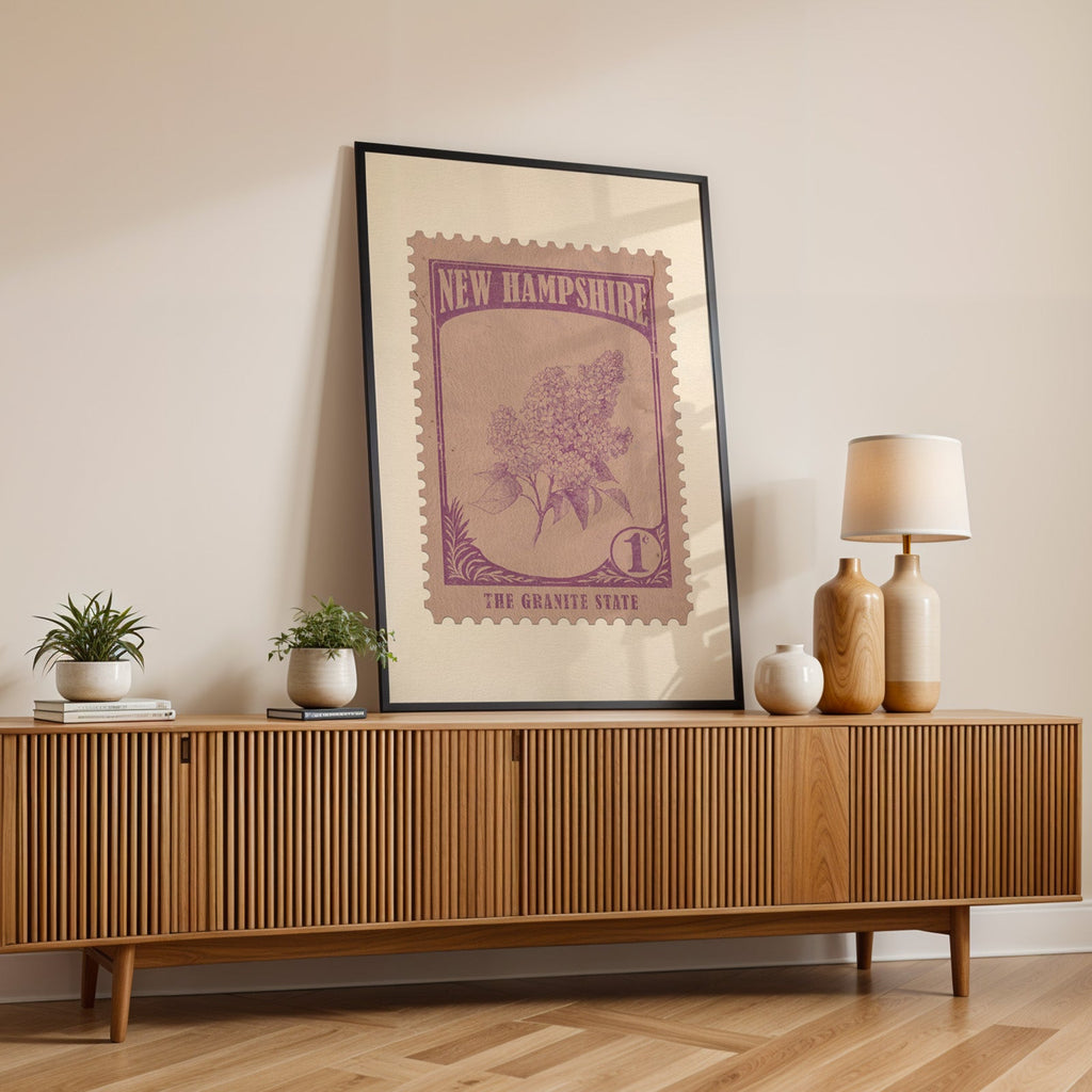 New Hampshire state flower print in a black frame leaning on a fluted wood credenza with vases and a lamp