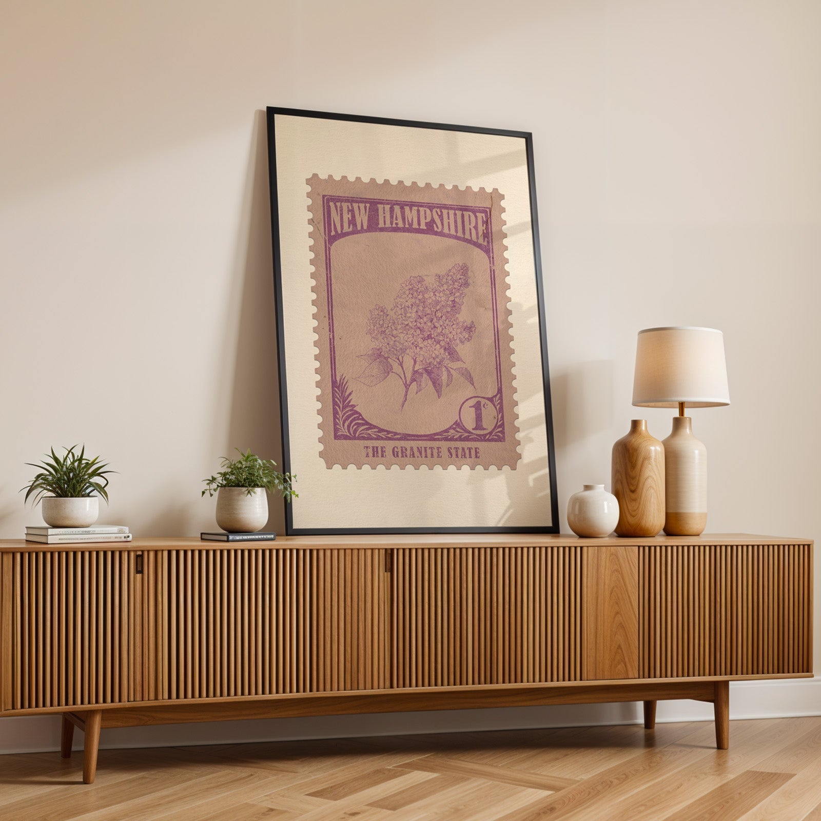 New Hampshire state flower print in a black frame leaning on a fluted wood credenza with vases and a lamp
