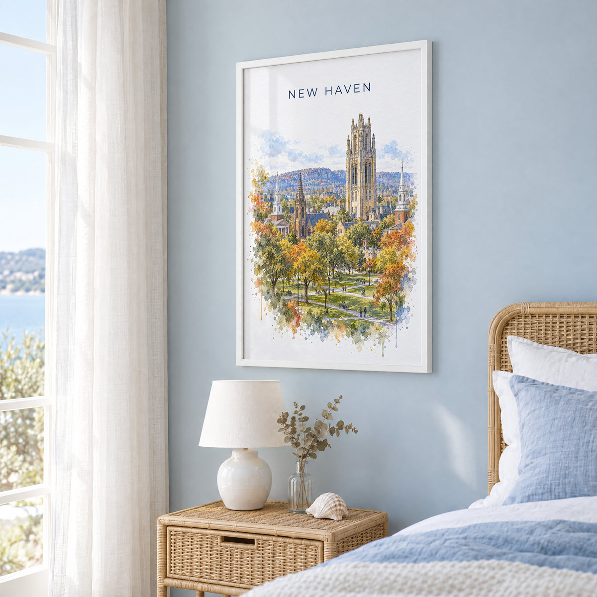 New Haven watercolor print in a white frame on a pale blue wall beside a rattan bed in a coastal bedroom