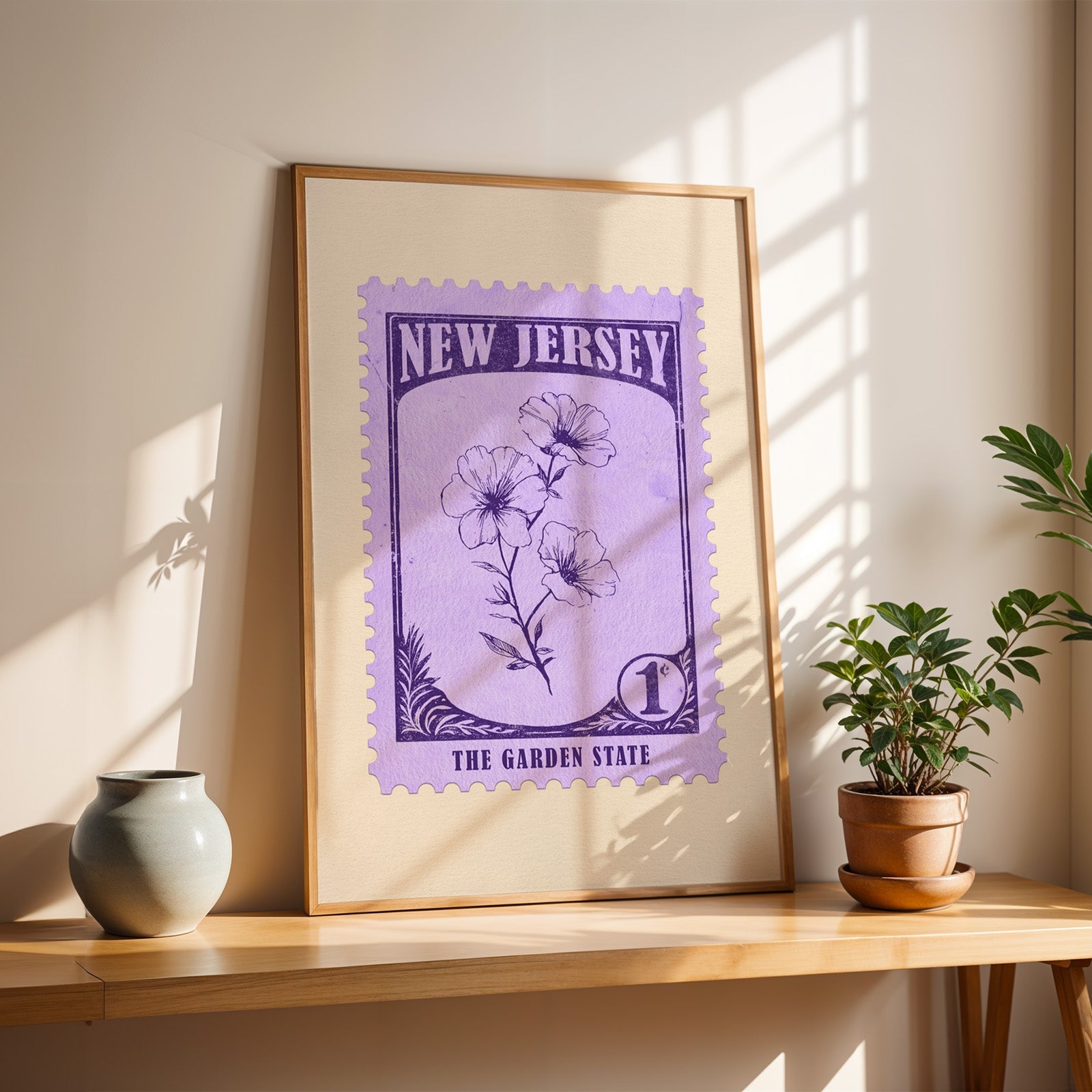 New Jersey violet stamp print in a light oak frame leaning on a wooden table beside a stoneware vase