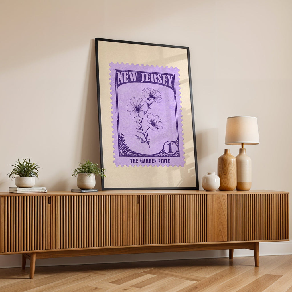 New Jersey state flower print in a black frame leaning on a fluted wood credenza with vases and a lamp
