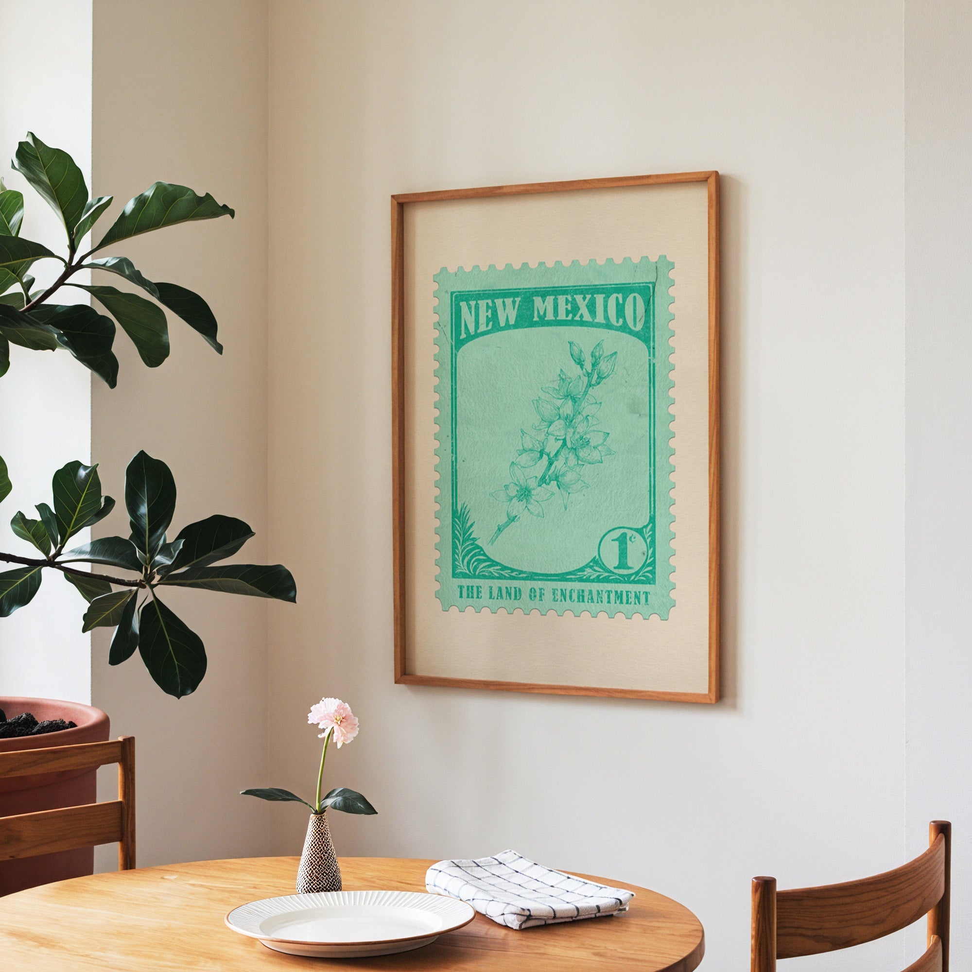 New Mexico state flower print framed above a round wooden table with a single bloom in a vase and books
