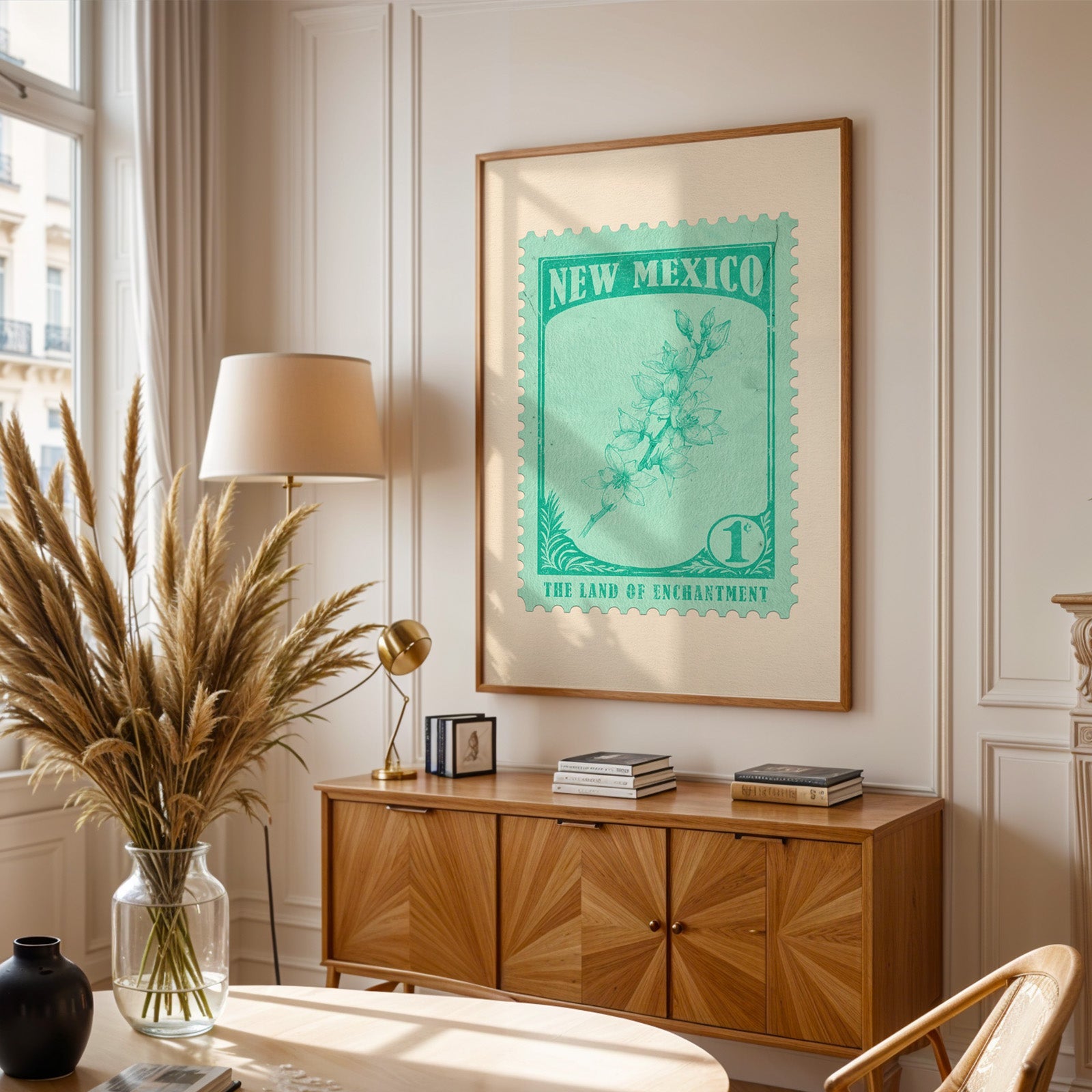New Mexico stamp print framed above a wooden sideboard, pampas grass in a glass vase and a floor lamp