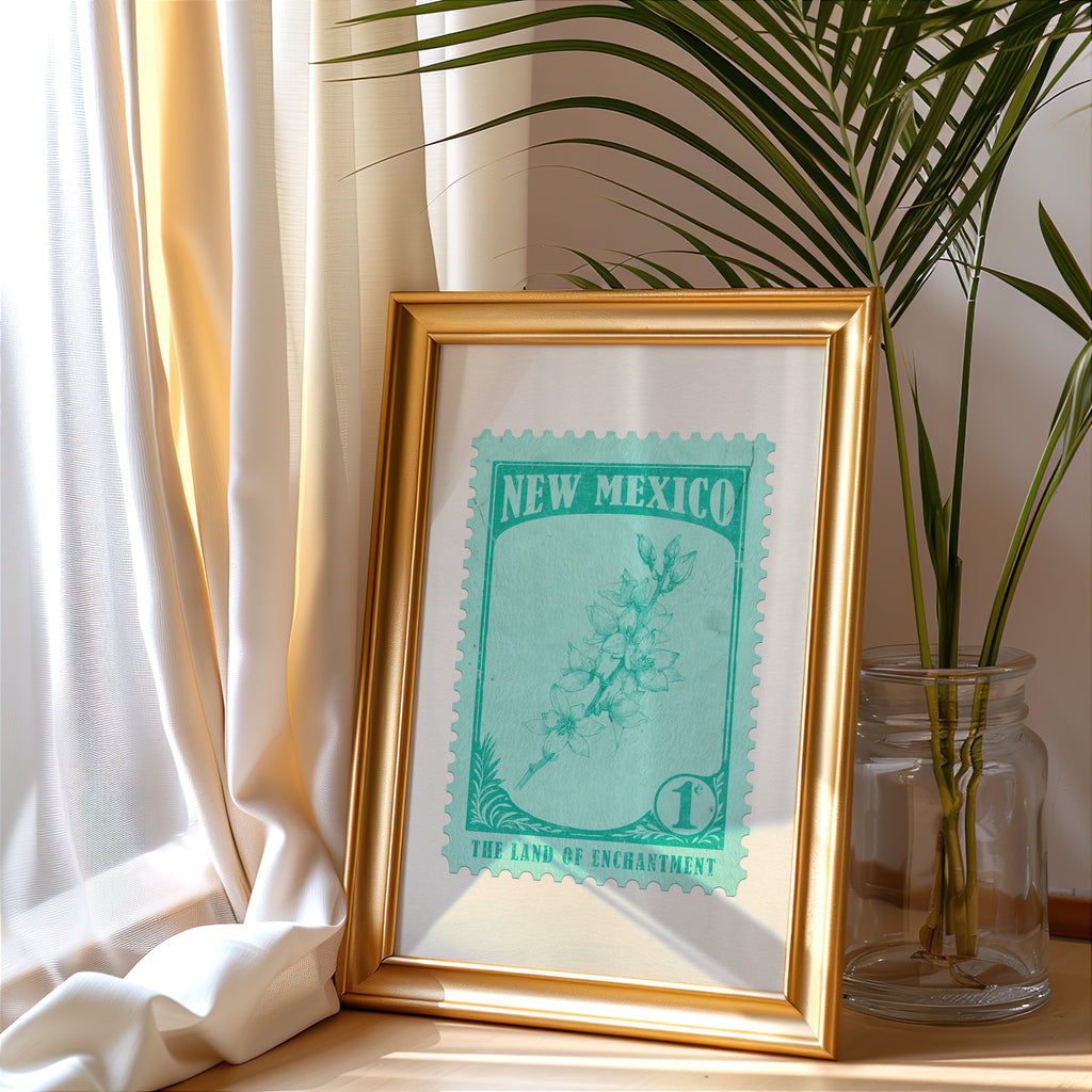 New Mexico stamp print in a gold frame leaning by a cream curtain with a palm in a glass jar