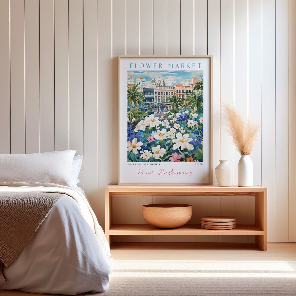 New Orleans flower market print in an oak frame on a wood bench against a white shiplap bedroom wall with pampas grass