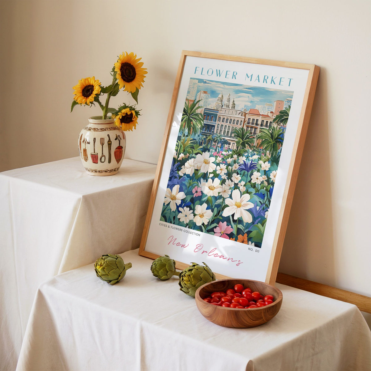 New Orleans flower market print in an oak frame leaning on a linen-draped table beside a vase of sunflowers