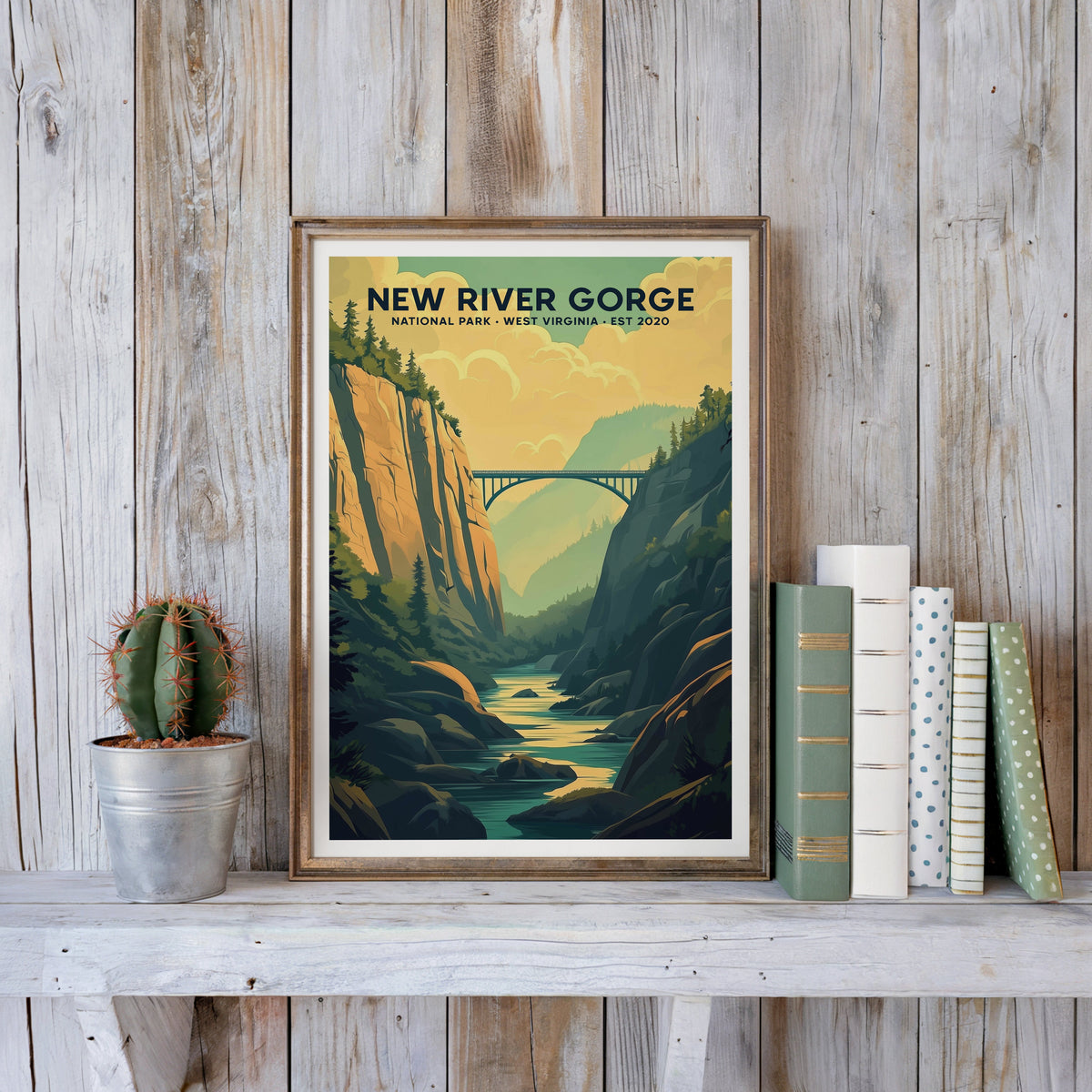 New River Gorge poster in an antique gold frame against whitewashed planks beside books and a cactus