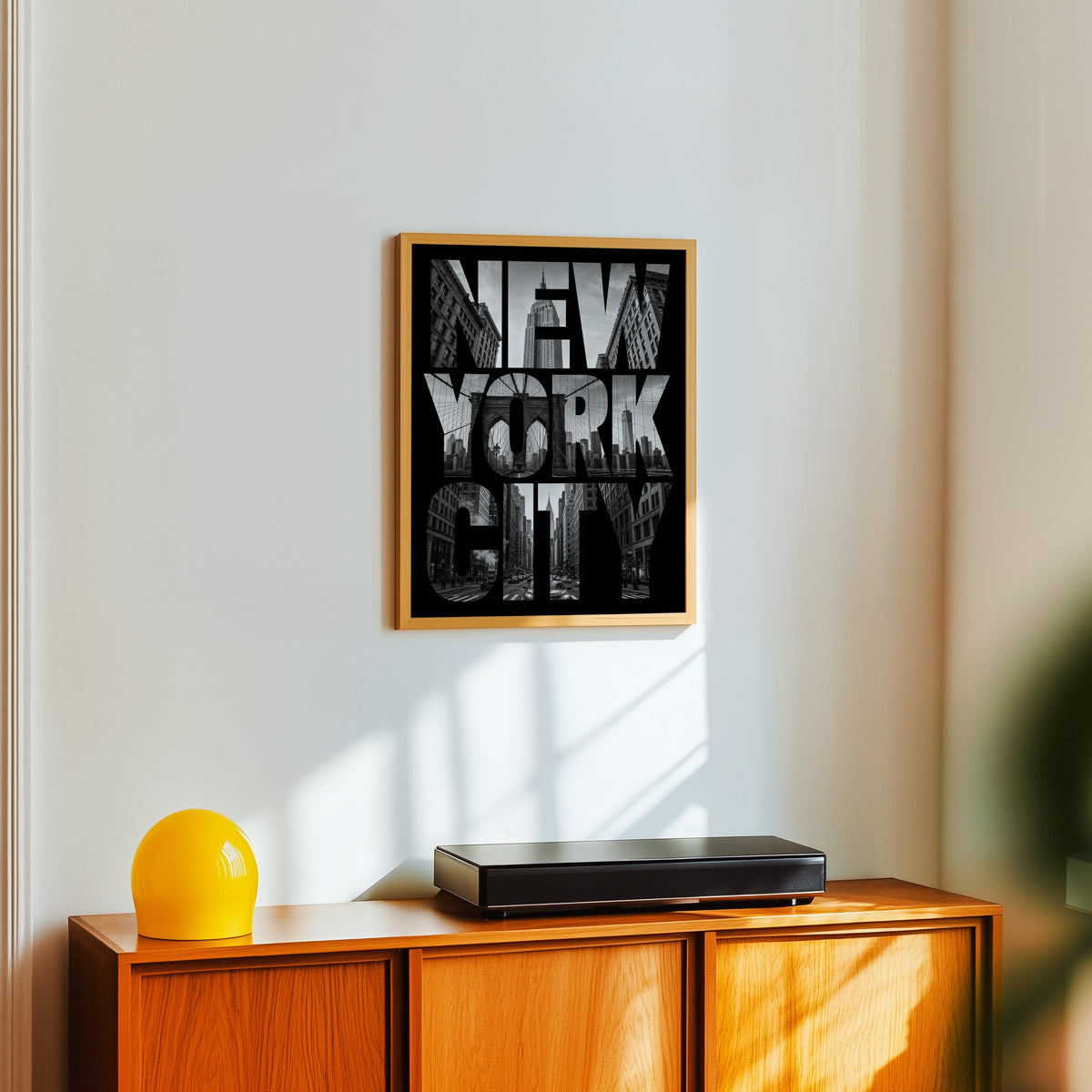 New York City letters filled with skyline photo print in an oak frame above a teak sideboard with a yellow glass lamp