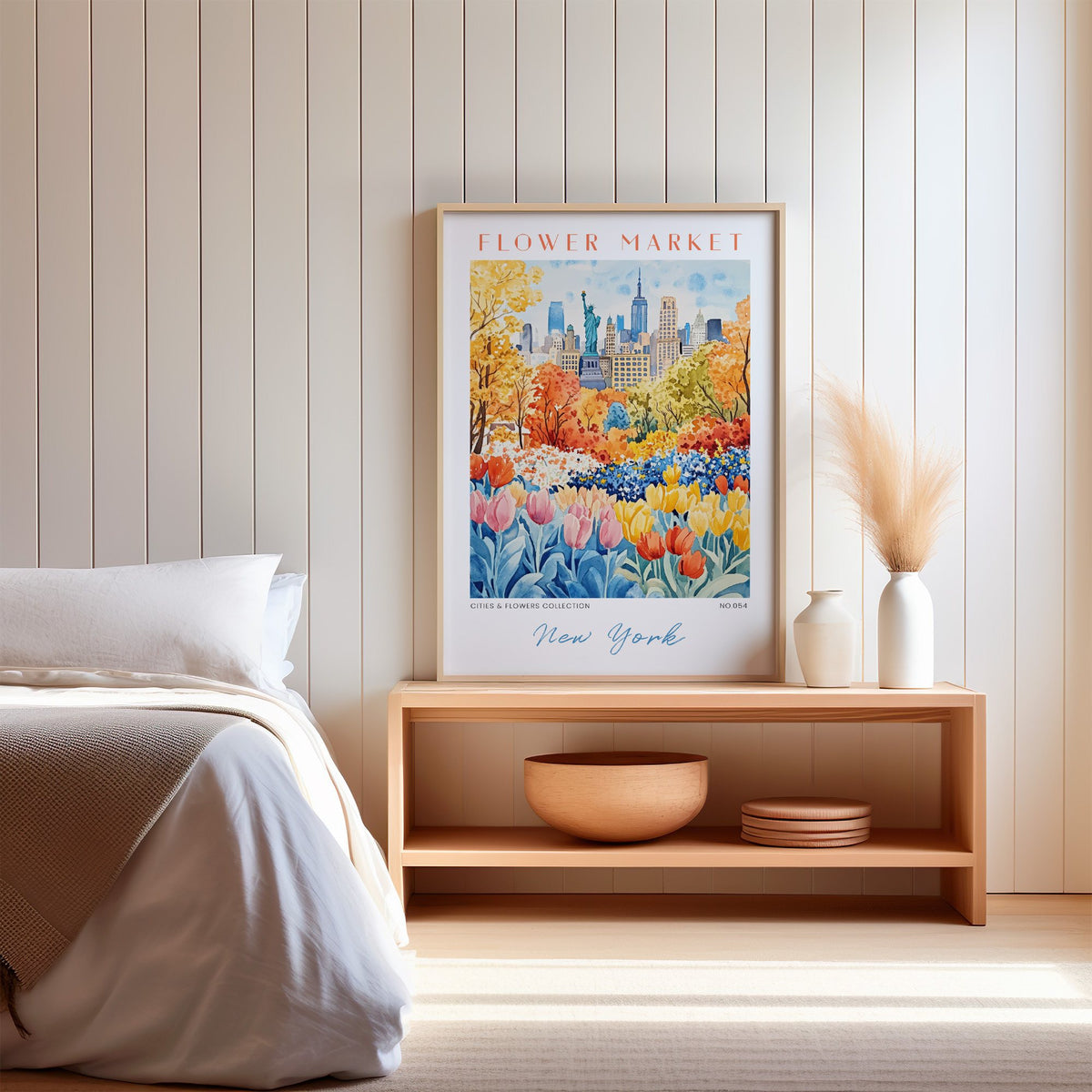New York flower market print in an oak frame on a wood bench against a white shiplap bedroom wall with pampas grass