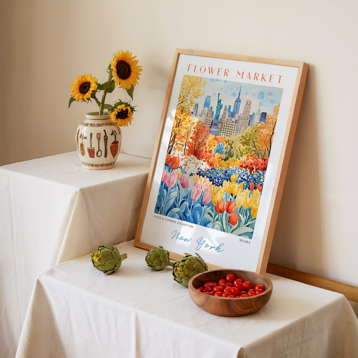 New York flower market print in an oak frame leaning on a linen-draped table beside a vase of sunflowers