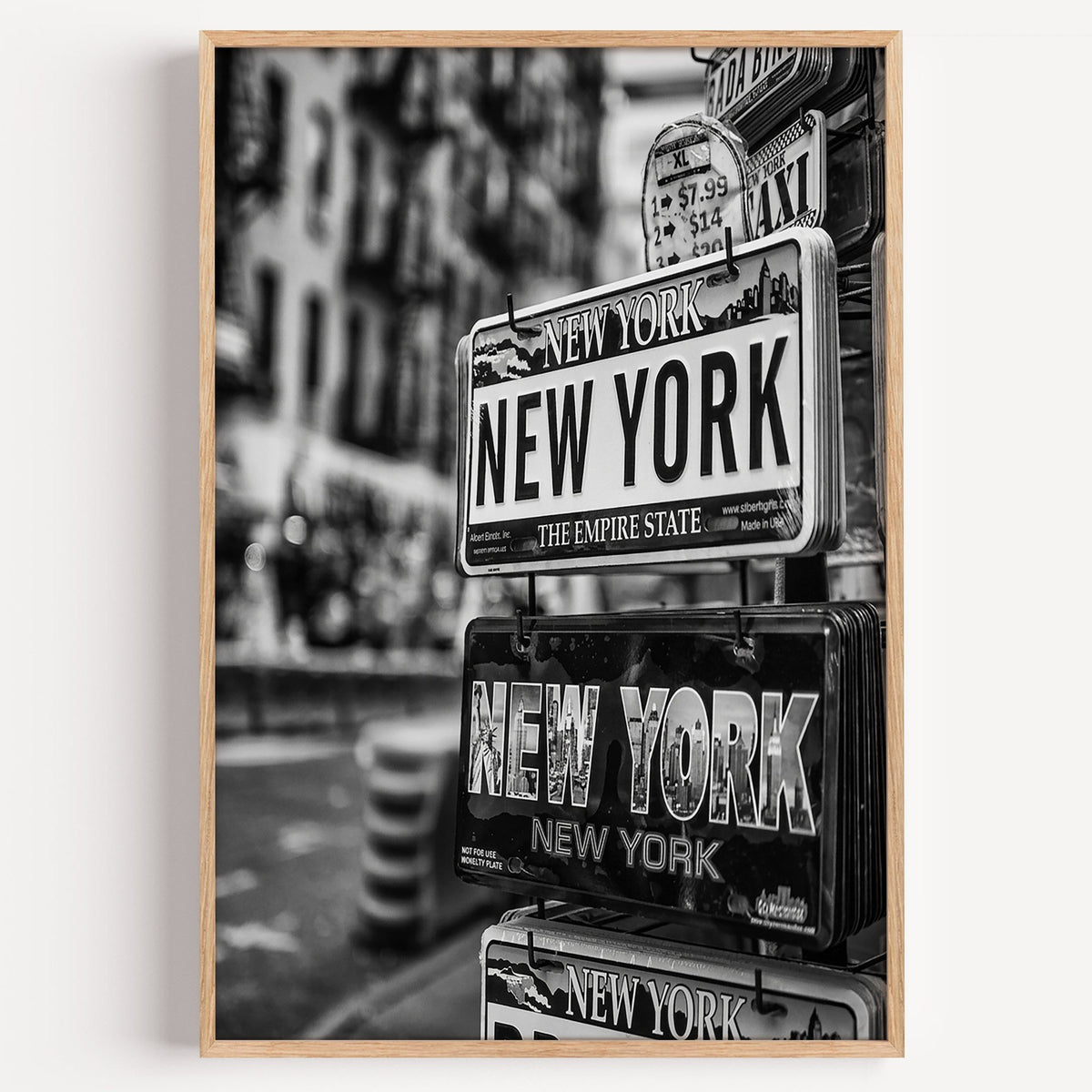 New York souvenir license plates on a rack print in a light oak frame on a plain white wall