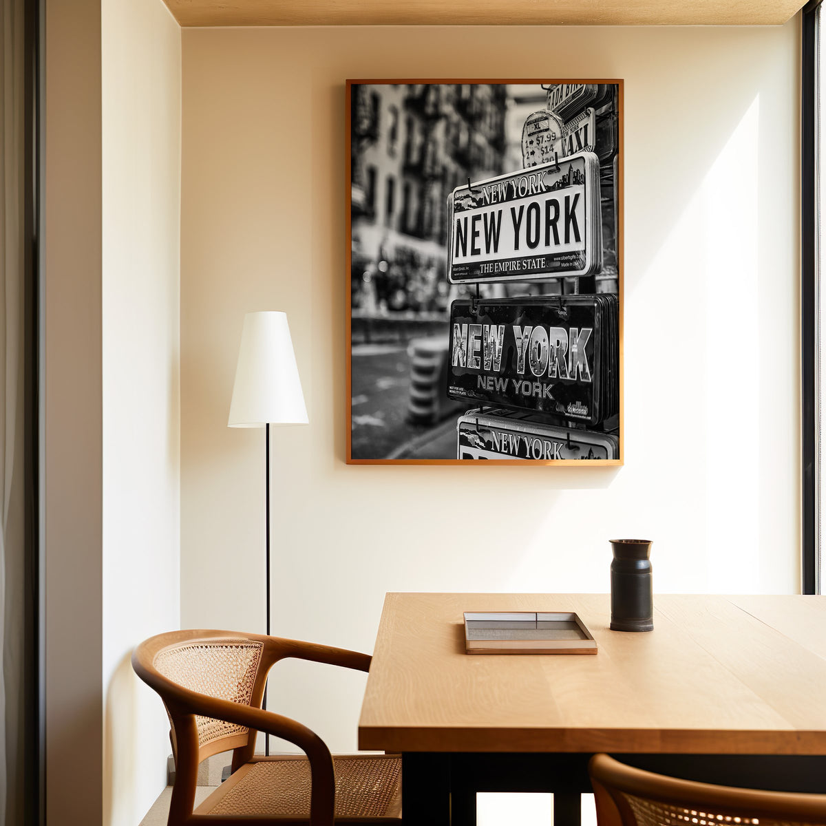 New York souvenir license plates on a rack print in an oak frame above a dining table and cane chair
