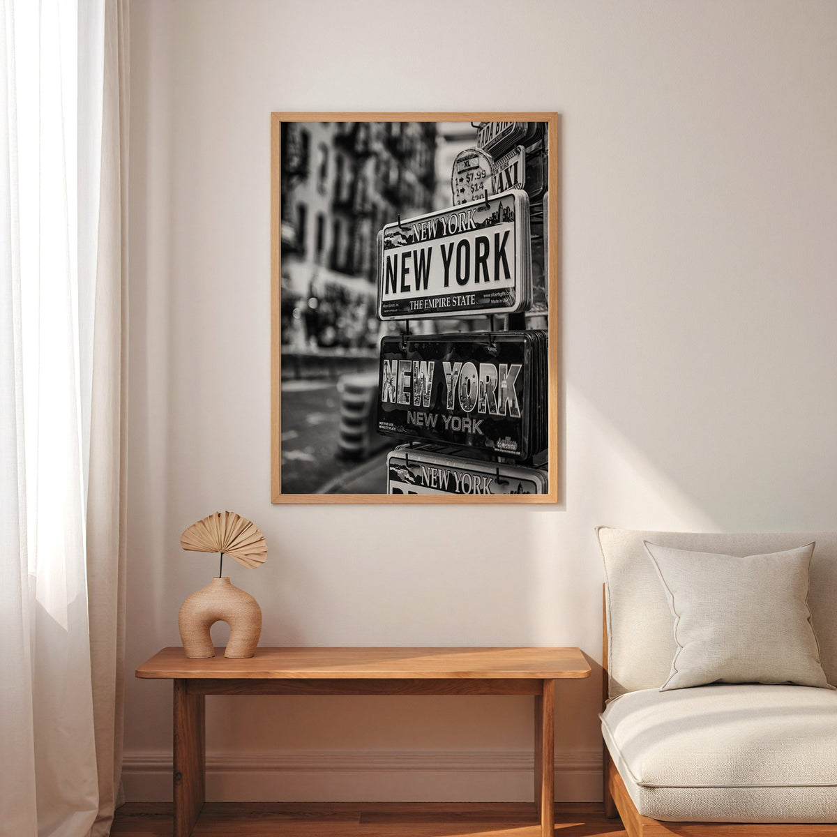 New York souvenir license plates on a rack print in an oak frame above a narrow console with an arched vase