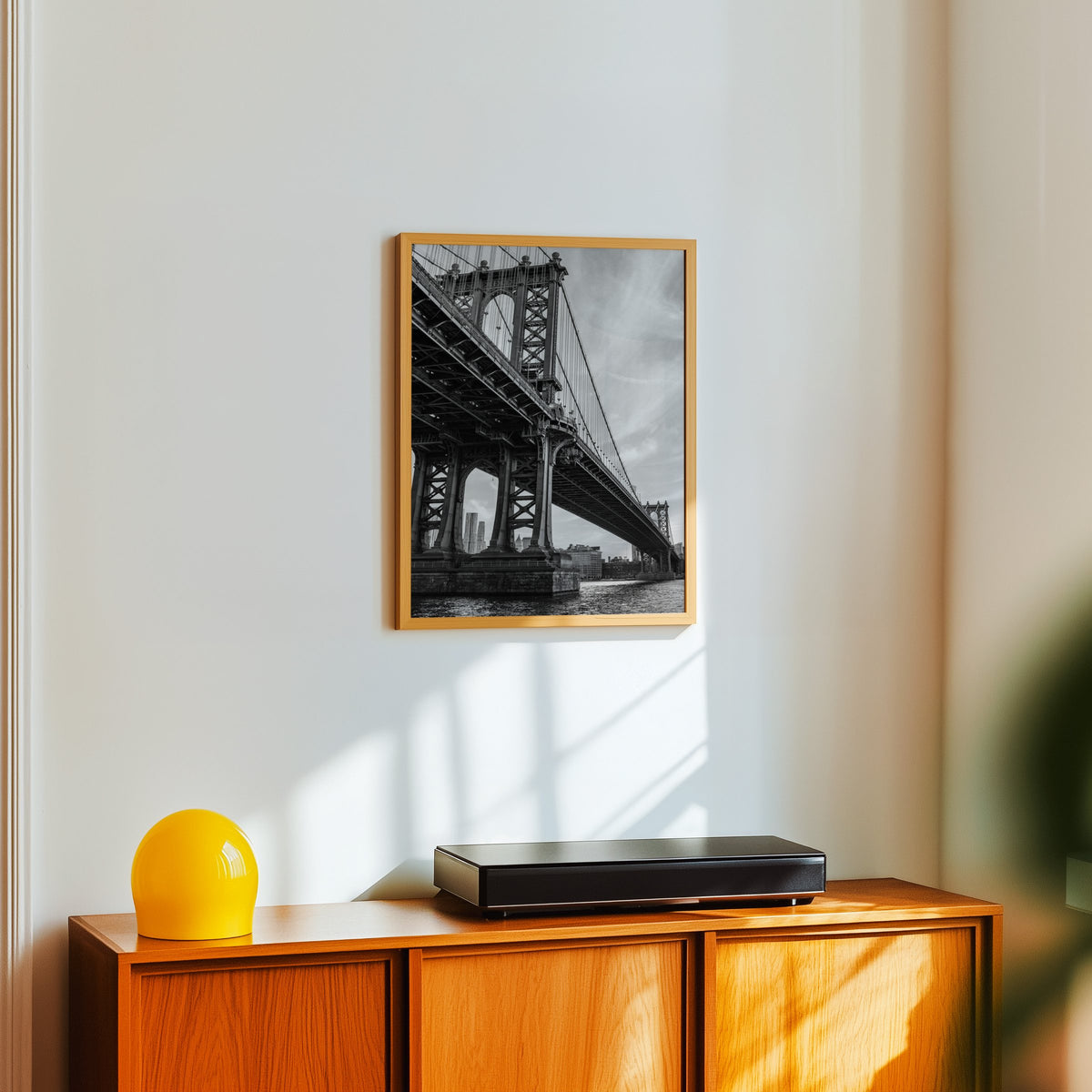 Manhattan Bridge underside from the river print in an oak frame above a teak sideboard with a yellow glass lamp