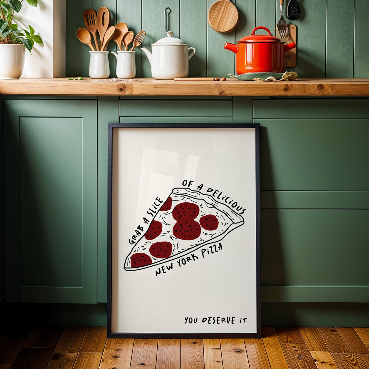 New York pizza slice print in a black frame against sage green kitchen cabinets