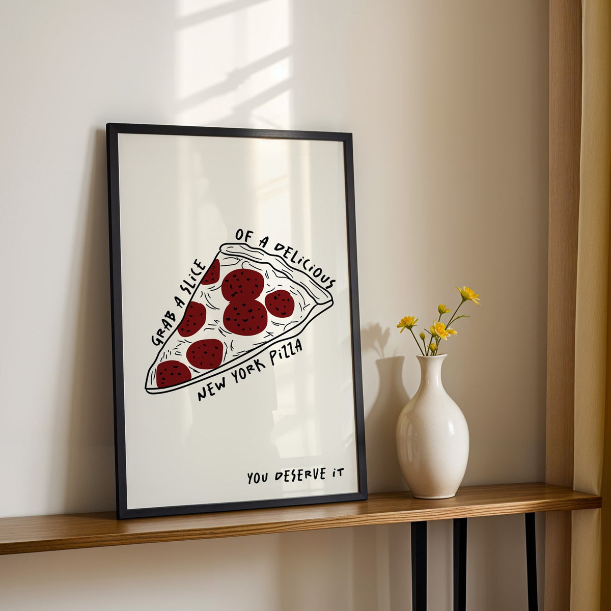 New York pizza slice print in a black frame on a console table with yellow daisies