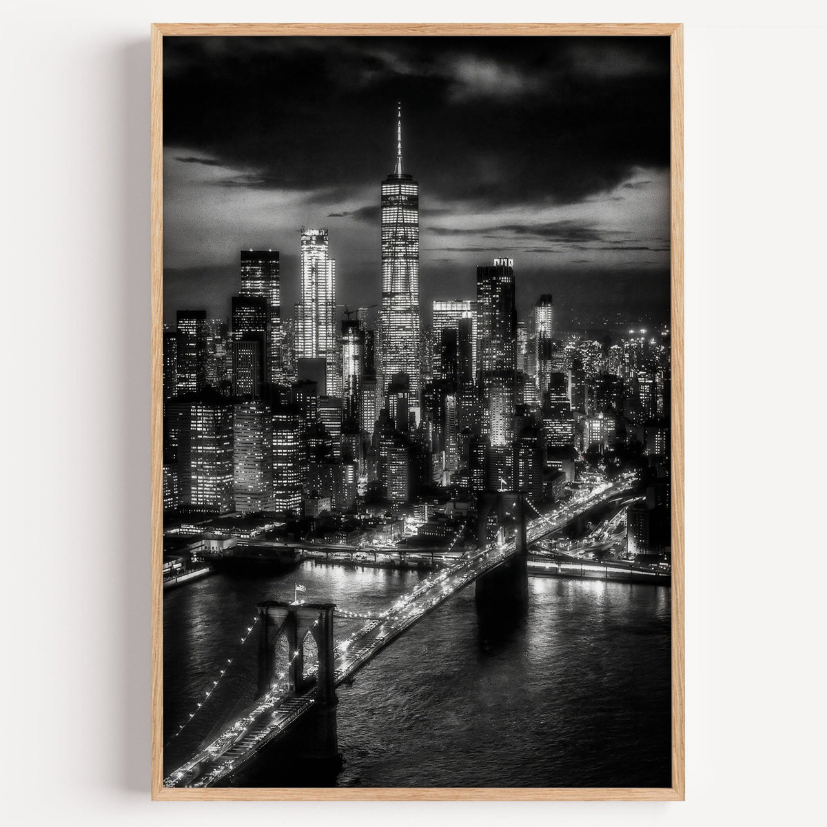 New York skyline at night with Brooklyn Bridge print in a light oak frame on a plain white wall