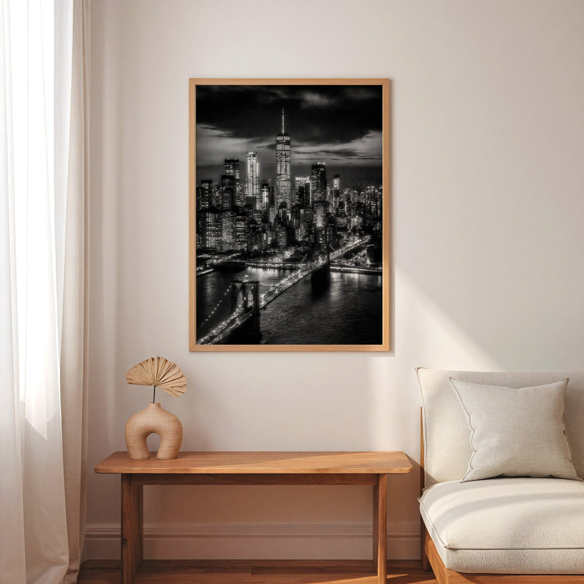 New York skyline at night with Brooklyn Bridge print in an oak frame above a narrow console with an arched vase