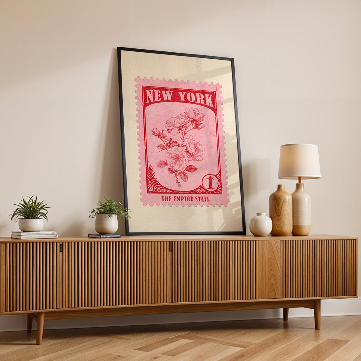 New York state flower print in a black frame leaning on a fluted wood credenza with vases and a lamp