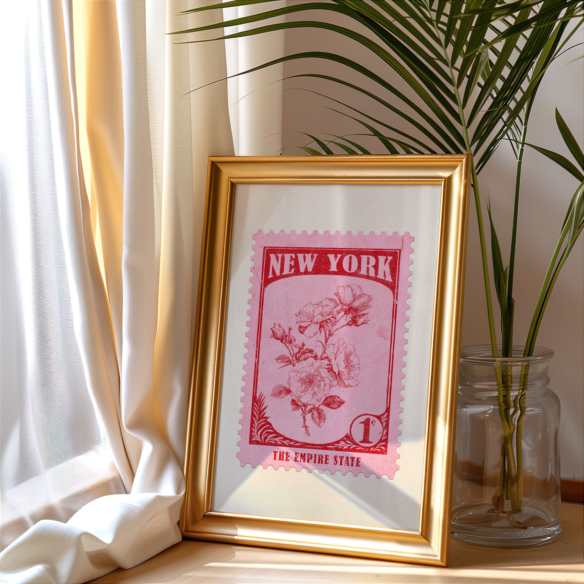 New York stamp print in a gold frame leaning by a cream curtain with a palm in a glass jar