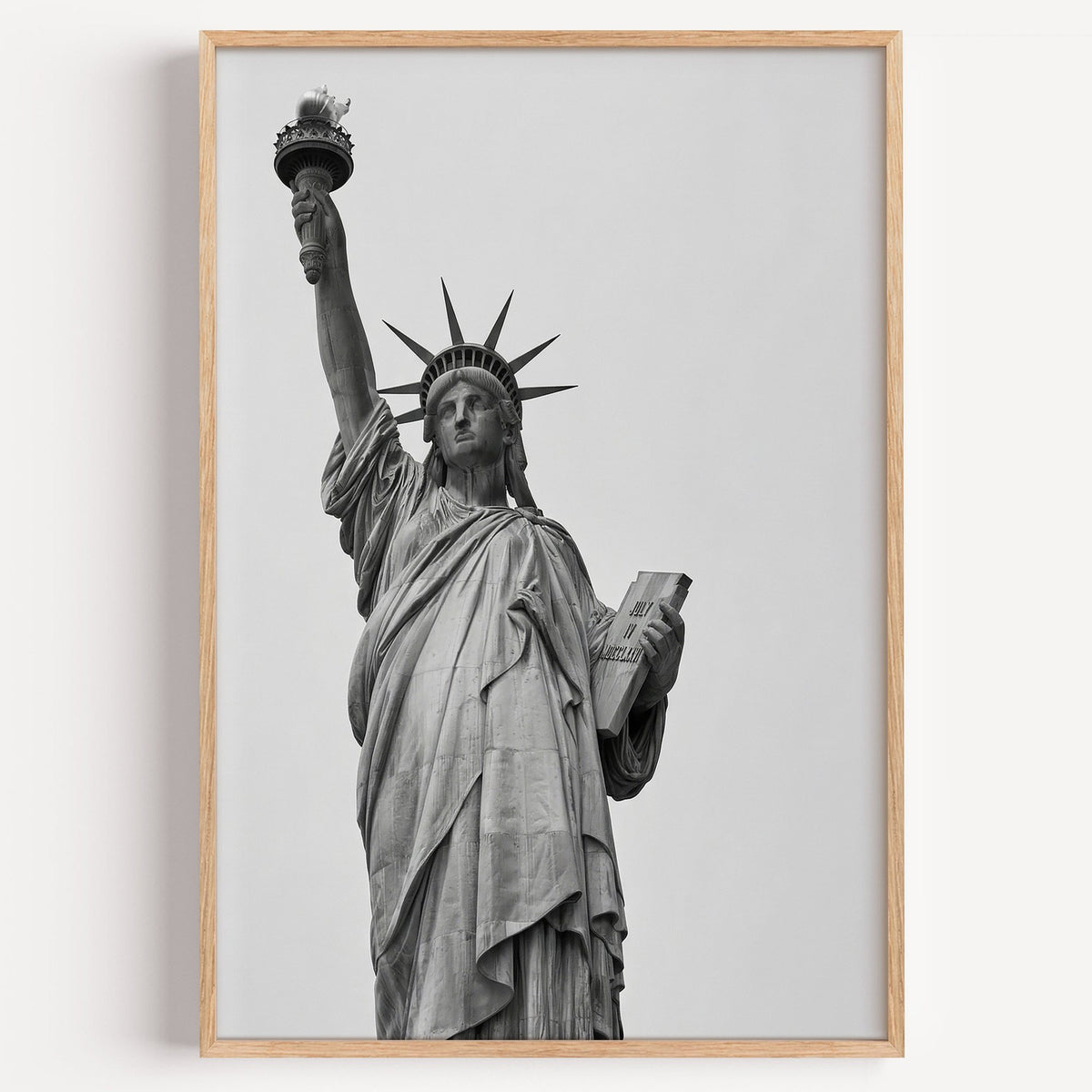 Statue of Liberty torch and tablet photo print in a light oak frame on a plain white wall