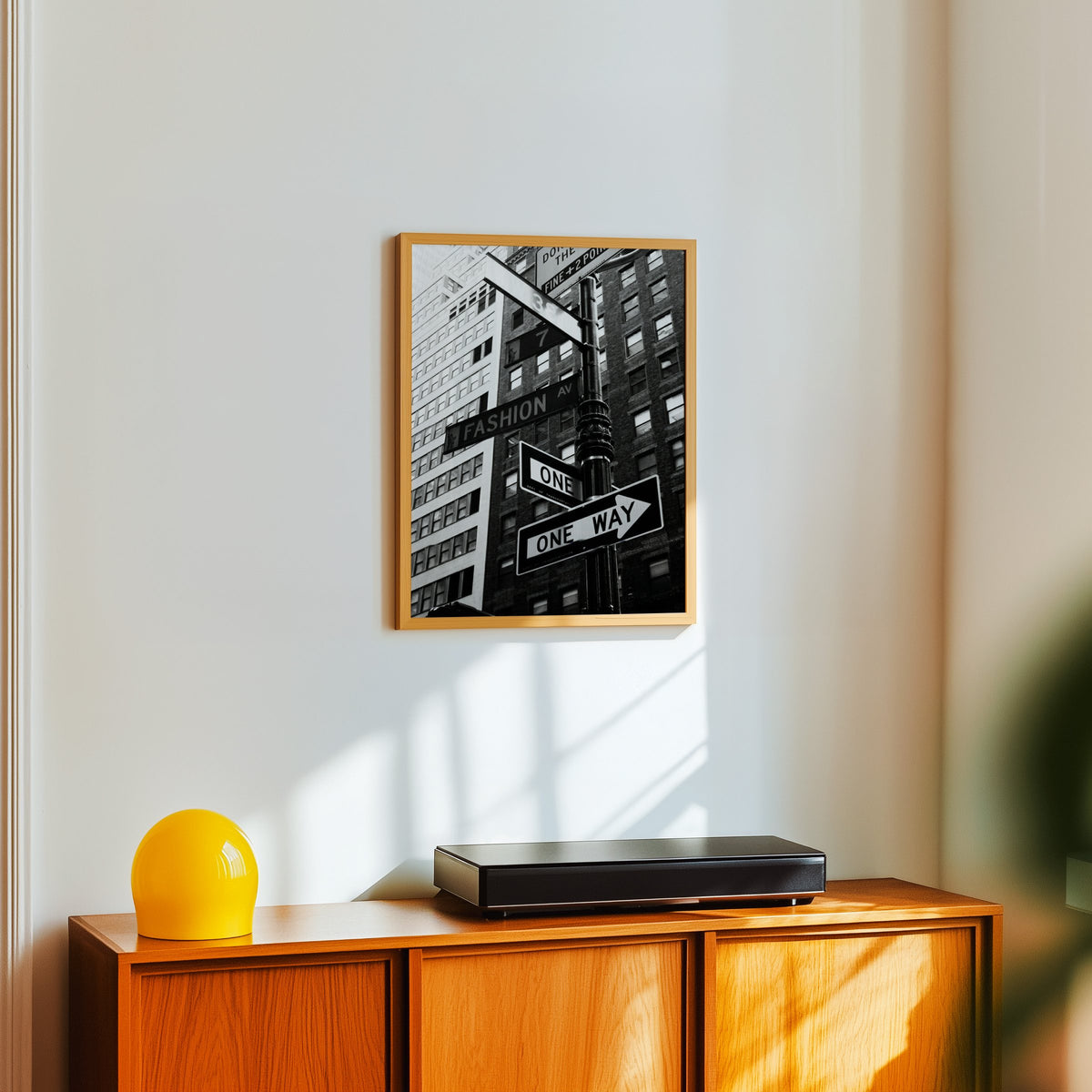 New York street sign pole with one way signs print in an oak frame above a teak sideboard with a yellow glass lamp