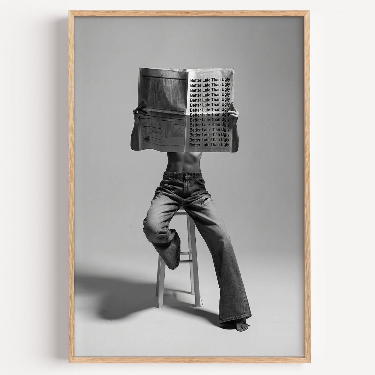 Figure on stool behind newspaper with repeated quote print in a light oak frame on a plain white wall