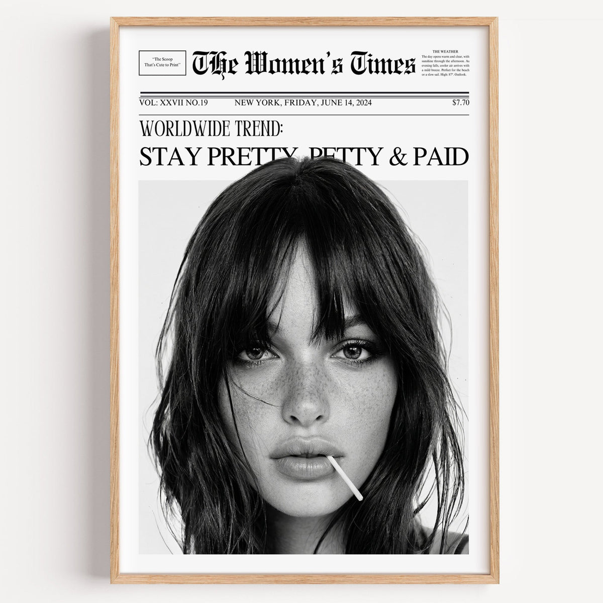 Mock front page with close-up of woman and lollipop print in a light oak frame on a plain white wall