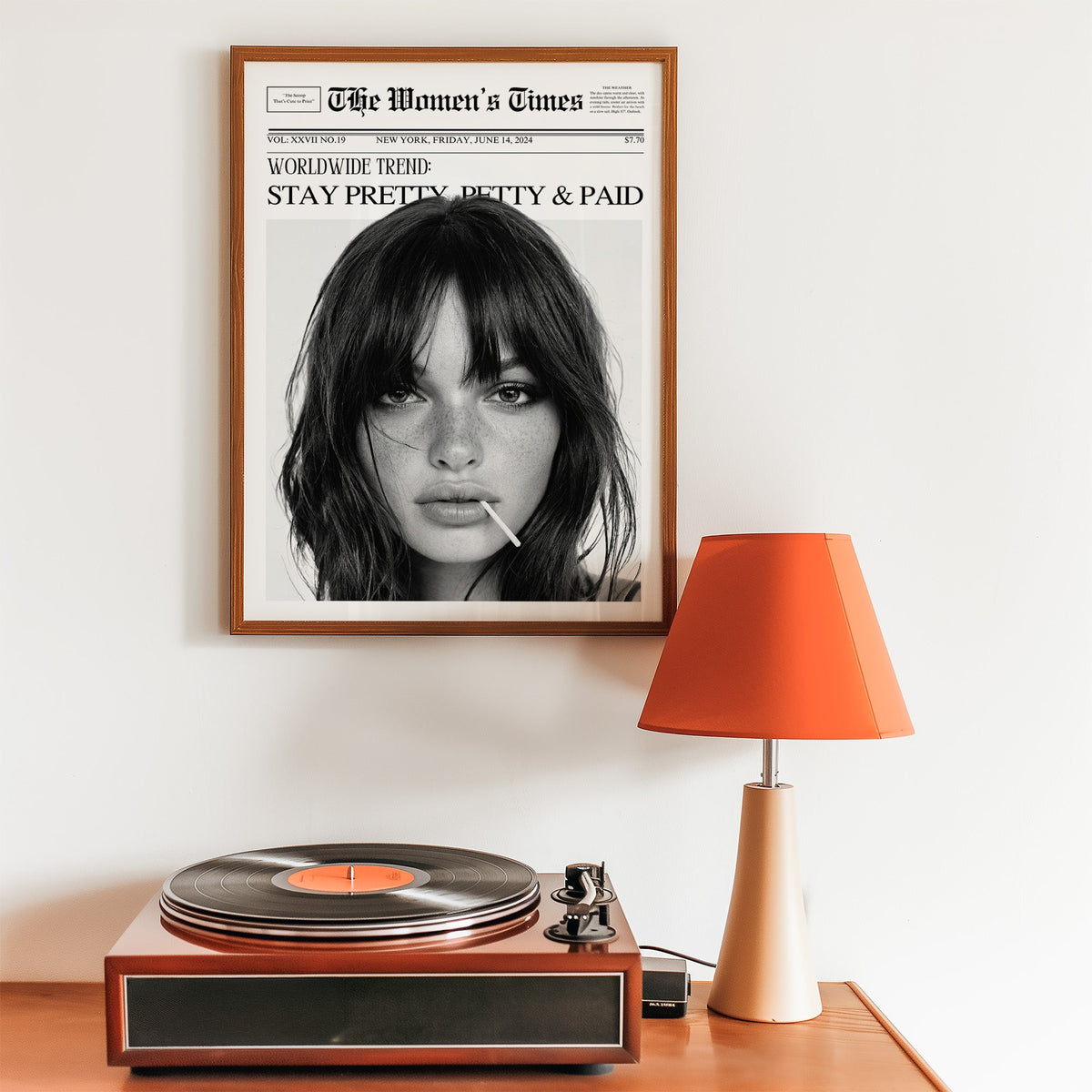 Mock front page with close-up of woman and lollipop print in a walnut frame above a record player and orange lamp
