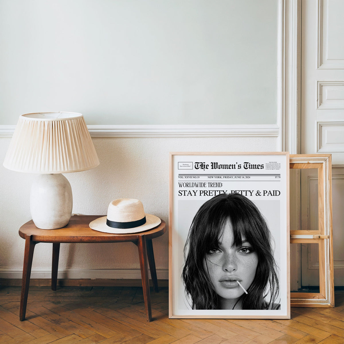 Mock front page with close-up of woman and lollipop print in a pine frame on a wood floor beside a lamp and straw hat