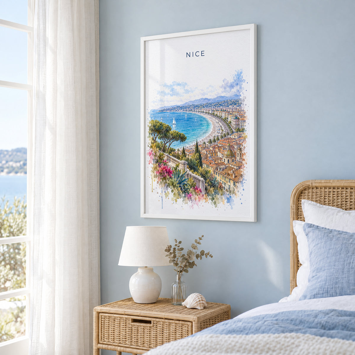 Nice, France watercolor print in a white frame on a pale blue wall beside a rattan bed in a coastal bedroom