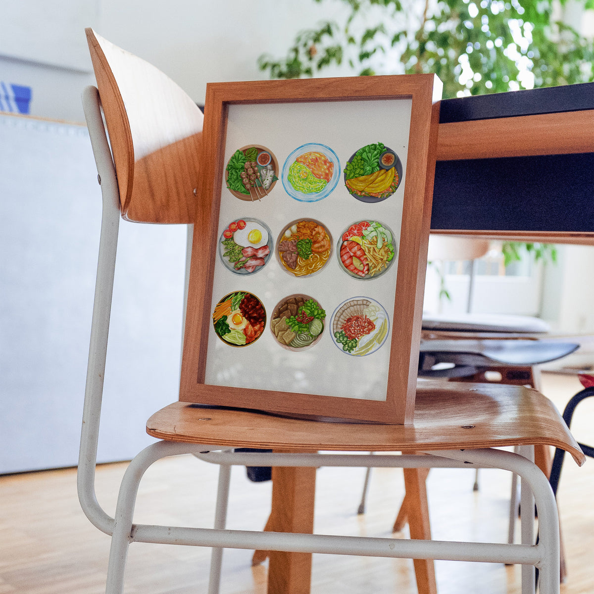 Nine plates food chart print in a walnut frame resting on a plywood studio chair beside a dark desk