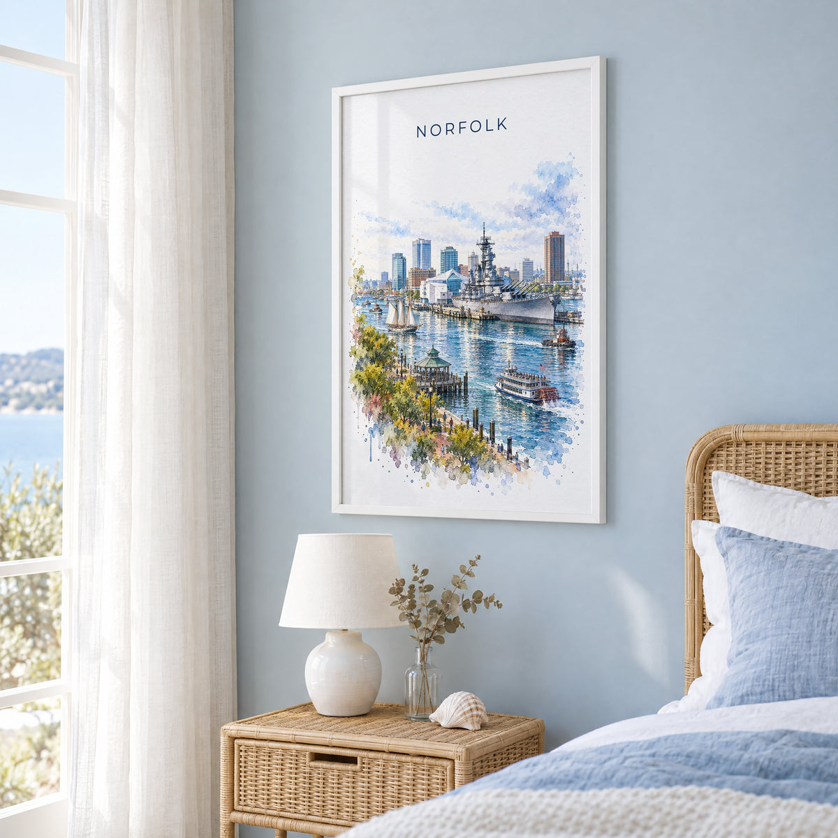 Norfolk, Virginia watercolor print in a white frame on a pale blue wall beside a rattan bed in a coastal bedroom
