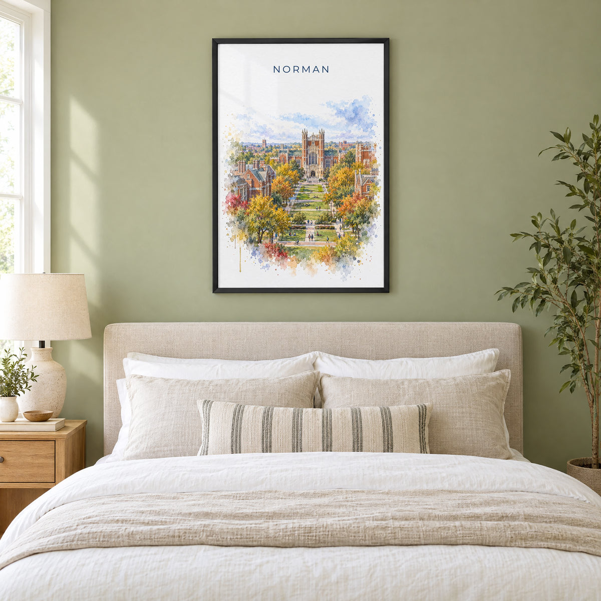 Norman, Oklahoma watercolor print in a black frame above an upholstered headboard in a sage green bedroom
