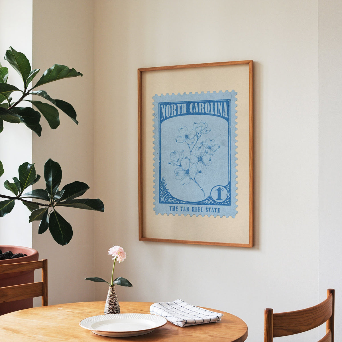 North Carolina state flower print framed above a round wooden table with a single bloom in a vase and books