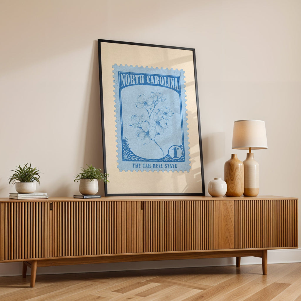 North Carolina state flower print in a black frame leaning on a fluted wood credenza with vases and a lamp