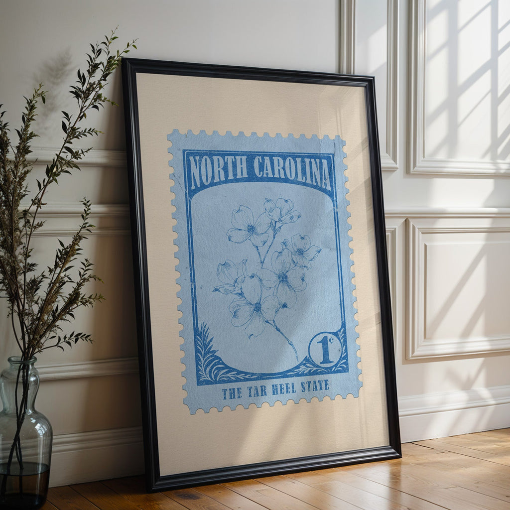 North Carolina state flower print in a black frame leaning against a white panelled wall beside olive branches