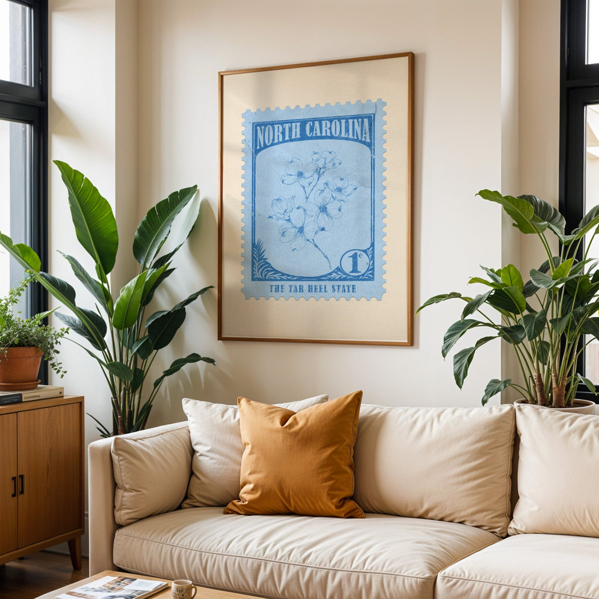 North Carolina state flower print framed above a cream sofa with an ochre cushion and large plants either side