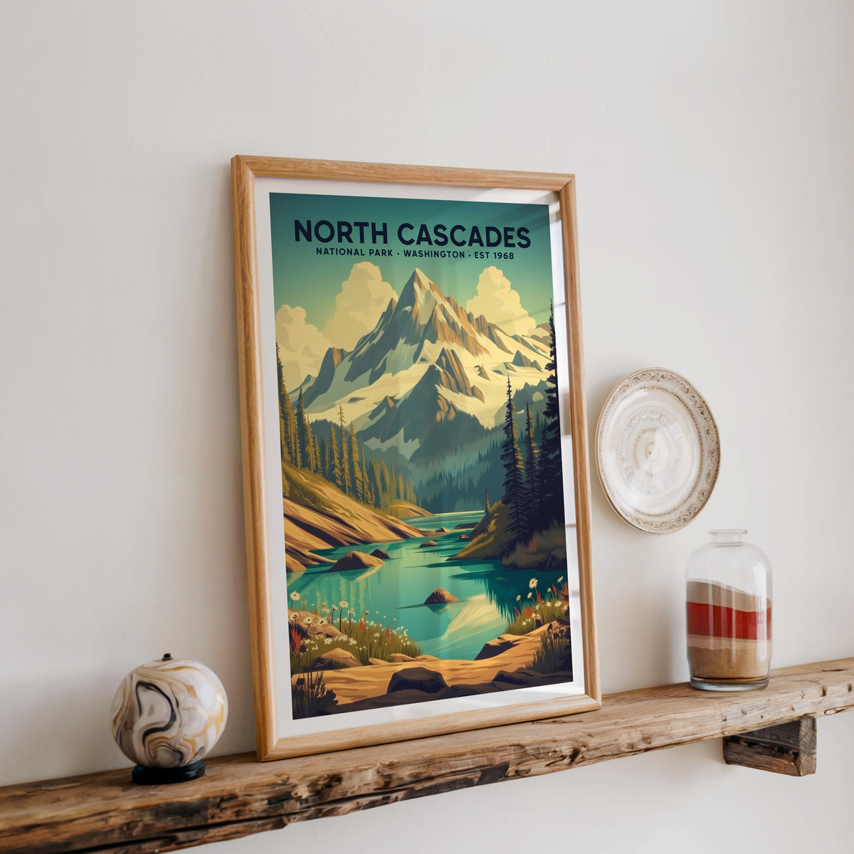North Cascades National Park print in an oak frame on a wood shelf with ceramics and a sand-filled jar