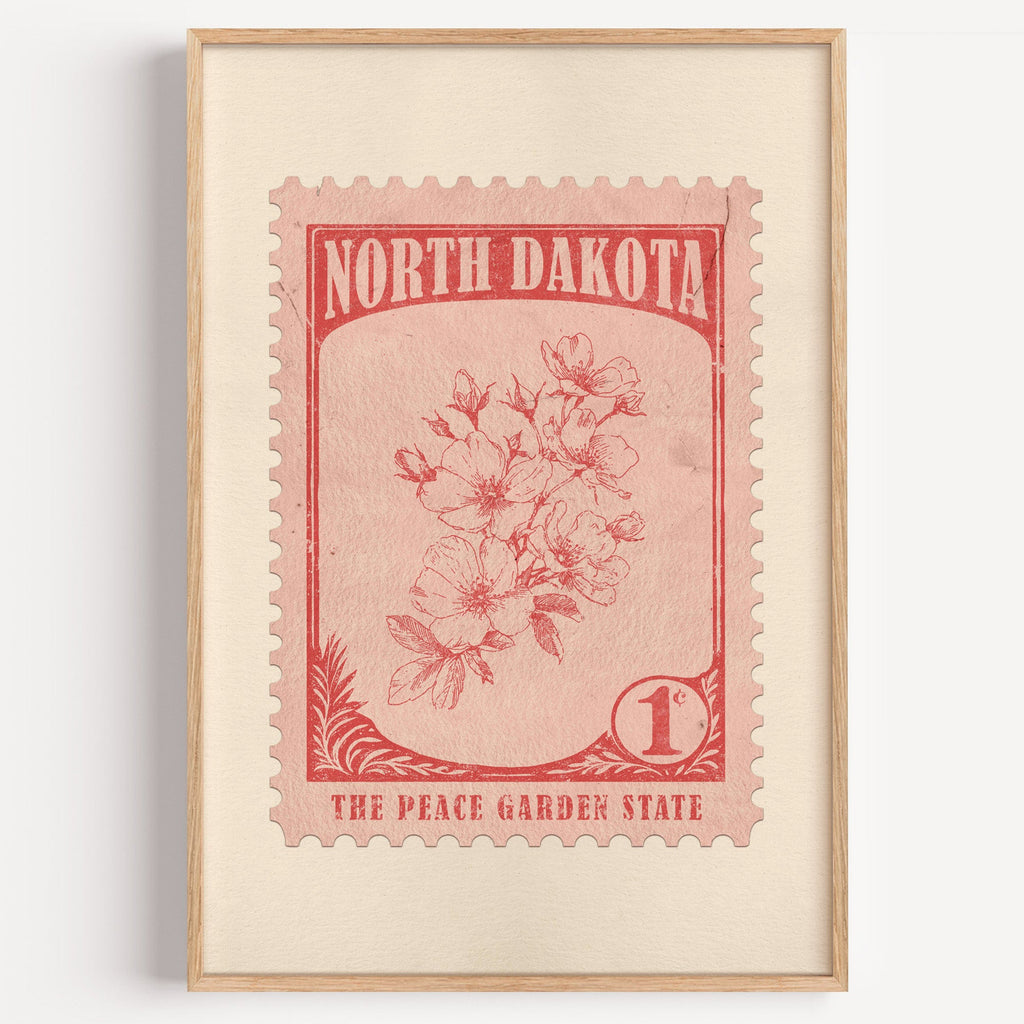 North Dakota state flower stamp print in brick red on blush, light oak frame on a plain white wall