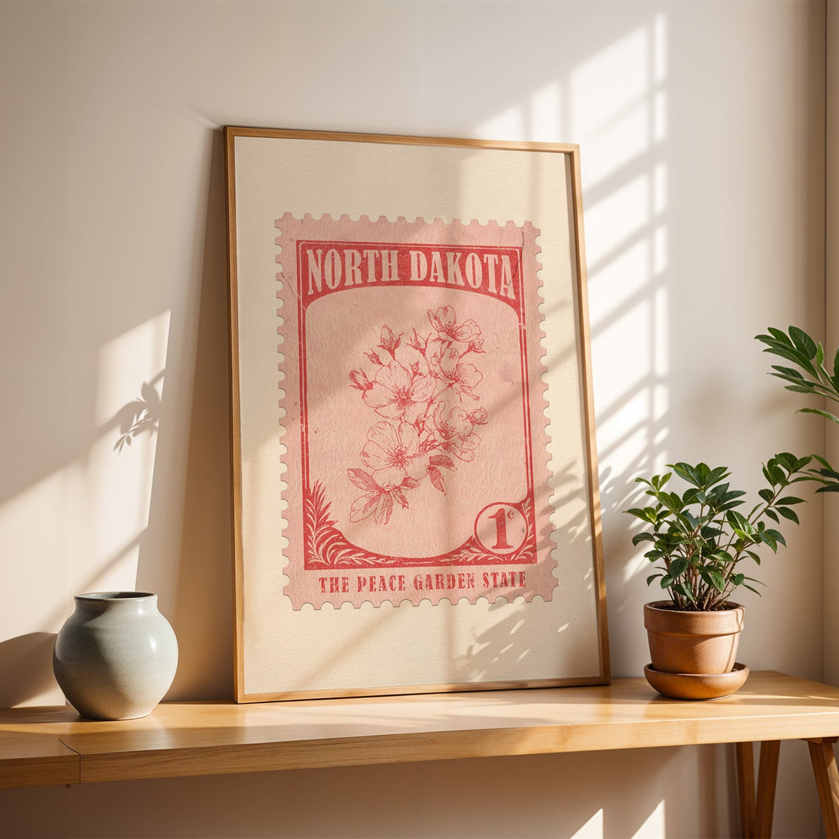 North Dakota Wild Prairie Rose stamp print in a light oak frame leaning on a wooden table beside a stoneware vase